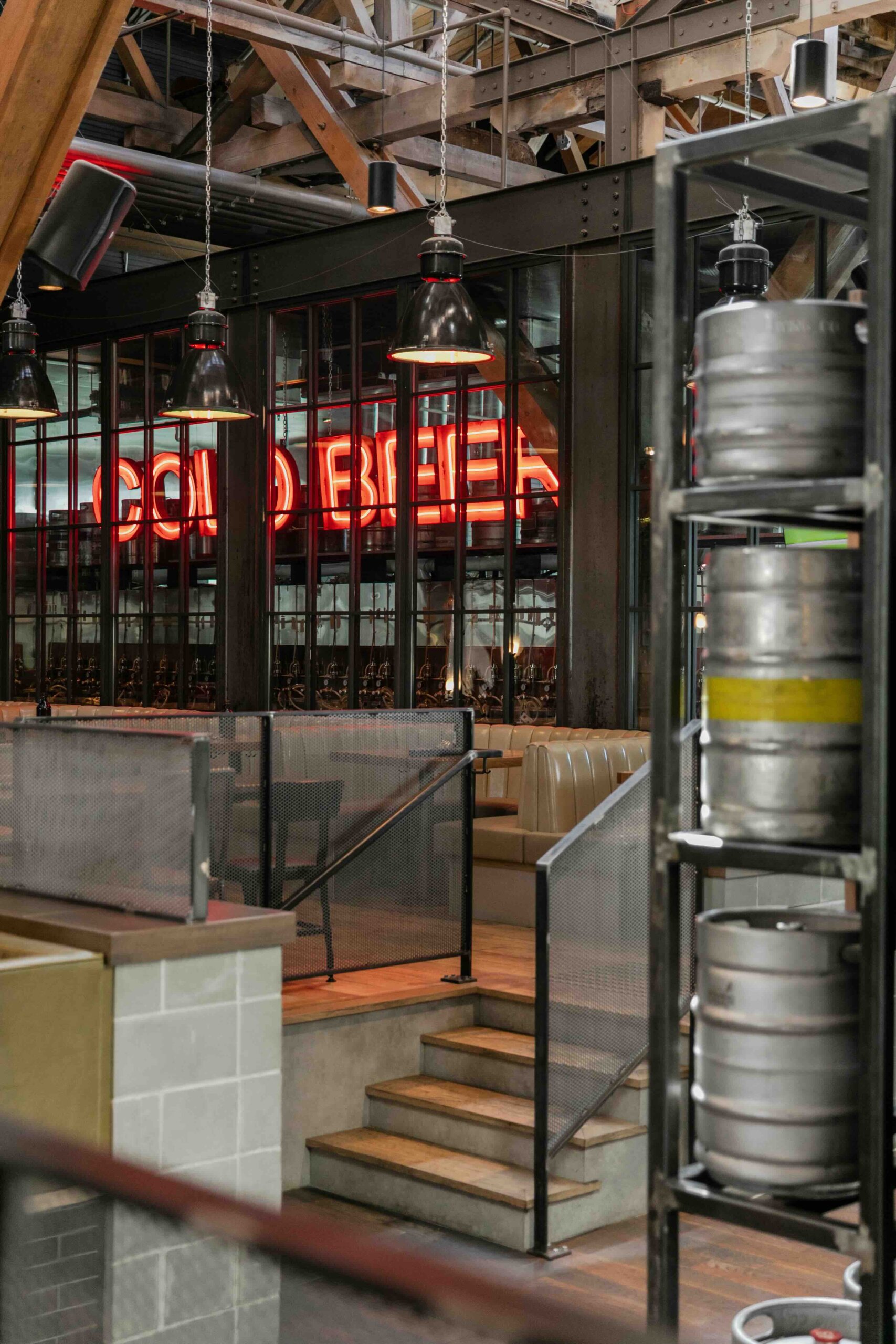 CRAFT Beer Market Interior of an industrial-style brewery or bar with metal fixtures, beer kegs stacked on shelves, and a red neon "Cold Beer" sign in the background—perfect for enjoying craft beer and casual dining with friends.