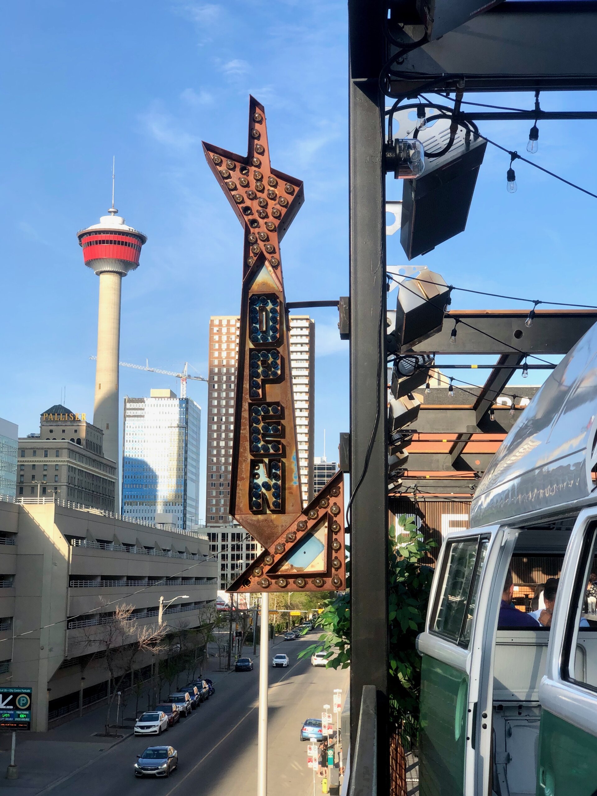 CRAFT Beer Market A retro vertical sign with "OPEN" letters stands above a city street, radiating Social Vibes, with the Calgary Tower and downtown buildings visible in the background.