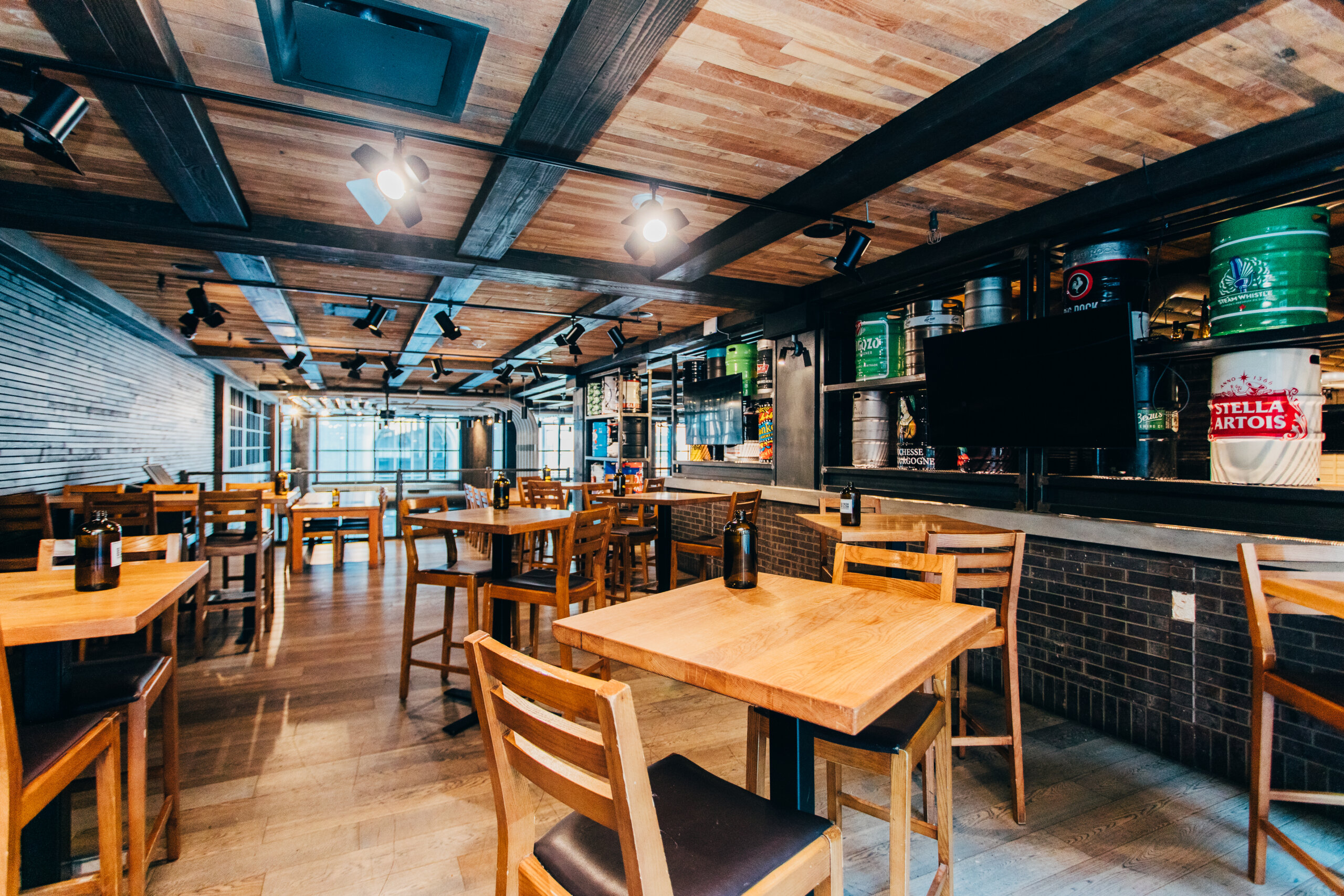 CRAFT Beer Market Spacious modern restaurant interior with wooden tables and chairs, exposed ceiling beams, and a bar area featuring craft beer on tap and bottles. Ideal for private events, this venue highlights locally sourced ingredients in every dish.