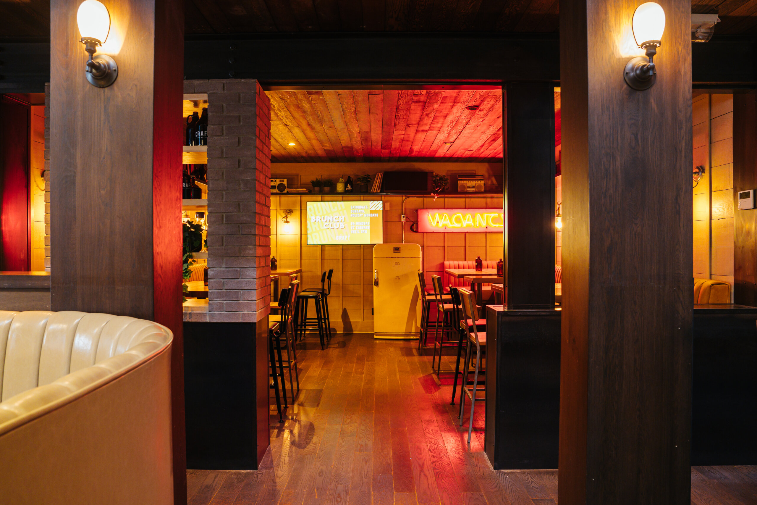CRAFT Beer Market Interior of a dimly lit restaurant with wooden floors, booths, bar stools, neon signs reading "VACANCY" and "SMASH BURGERS FRIES MILKSHAKES," and a lively atmosphere perfect for enjoying craft cocktails and social vibes.
