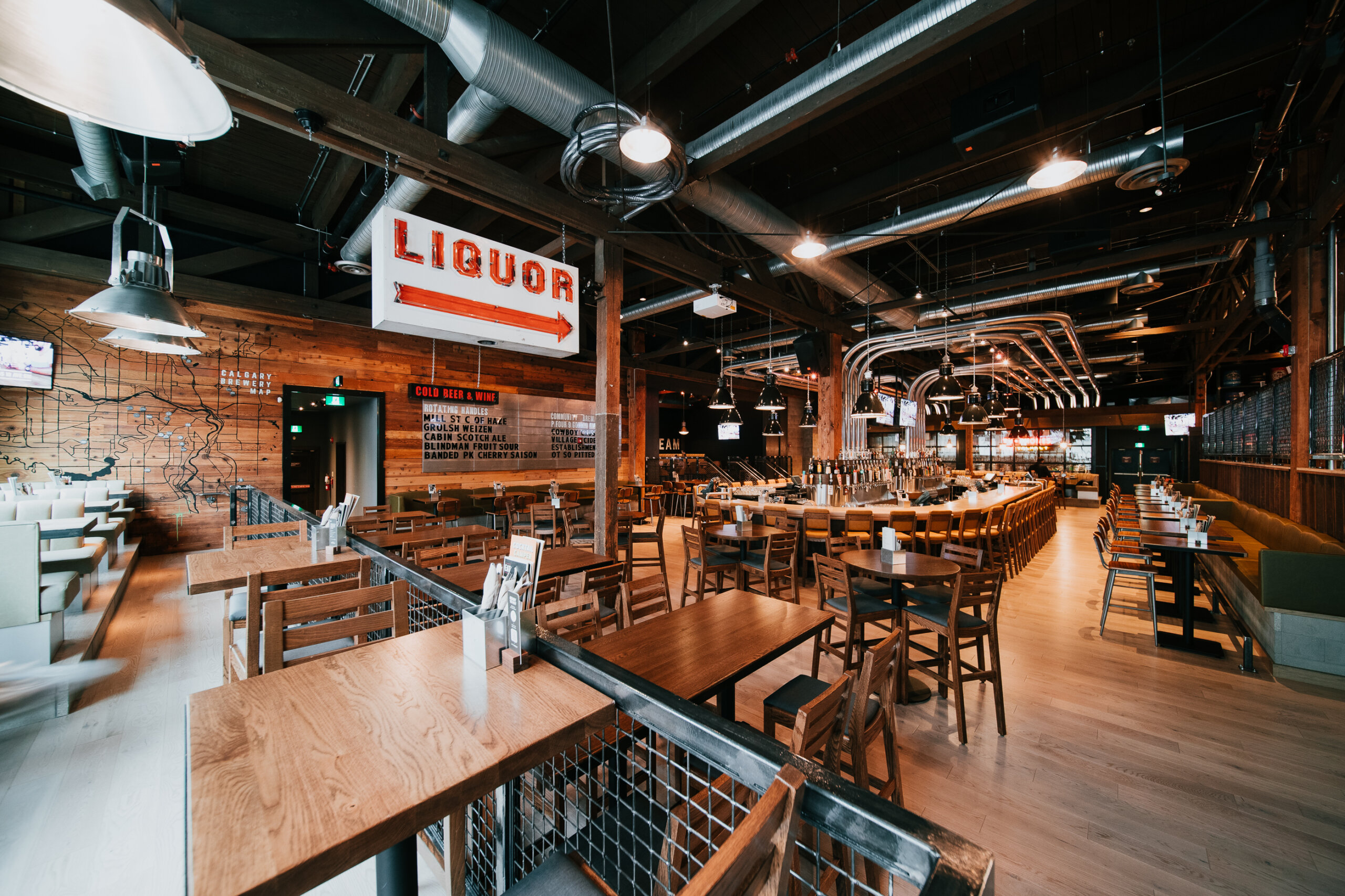 CRAFT Beer Market Spacious, modern bar and restaurant interior with wooden tables and chairs, industrial ceiling, a large "LIQUOR" sign on the wall, and inviting social vibes—perfect for enjoying craft cocktails.