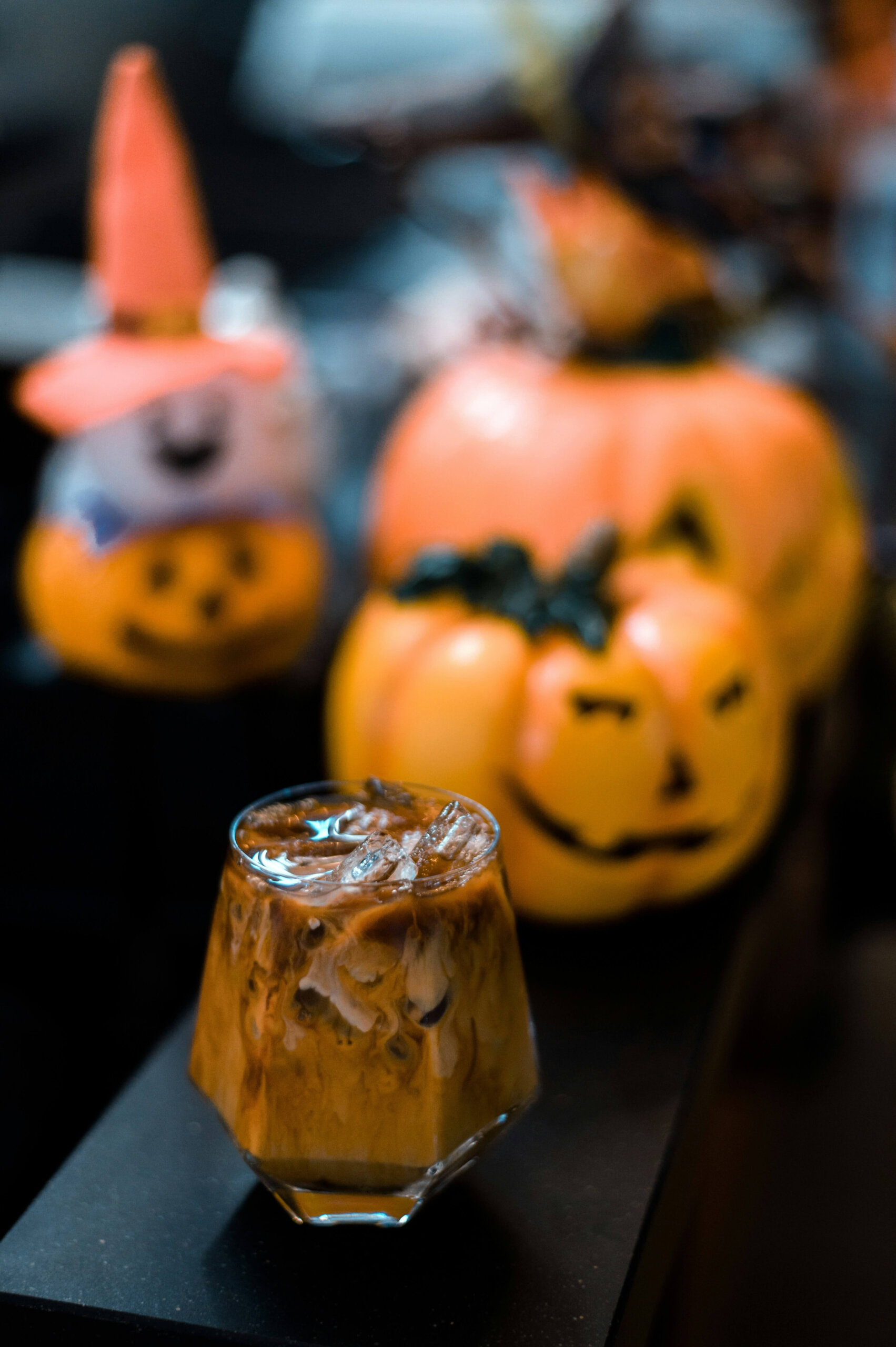 CRAFT Beer Market A glass of iced coffee sits in front of Halloween-themed pumpkin decorations with painted faces and a small witch hat, perfect for group bookings looking to celebrate together.