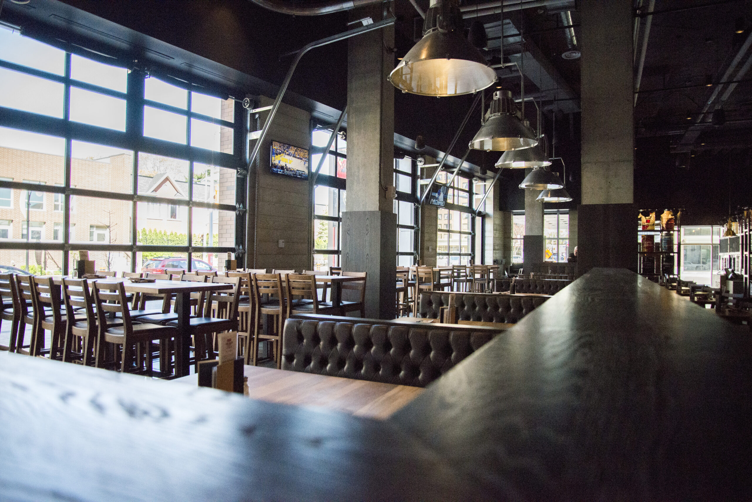 CRAFT Beer Market A spacious, modern restaurant interior with large windows, wooden tables and chairs, pendant lighting, a tufted booth along a wooden partition, and an inviting bar serving craft cocktails.