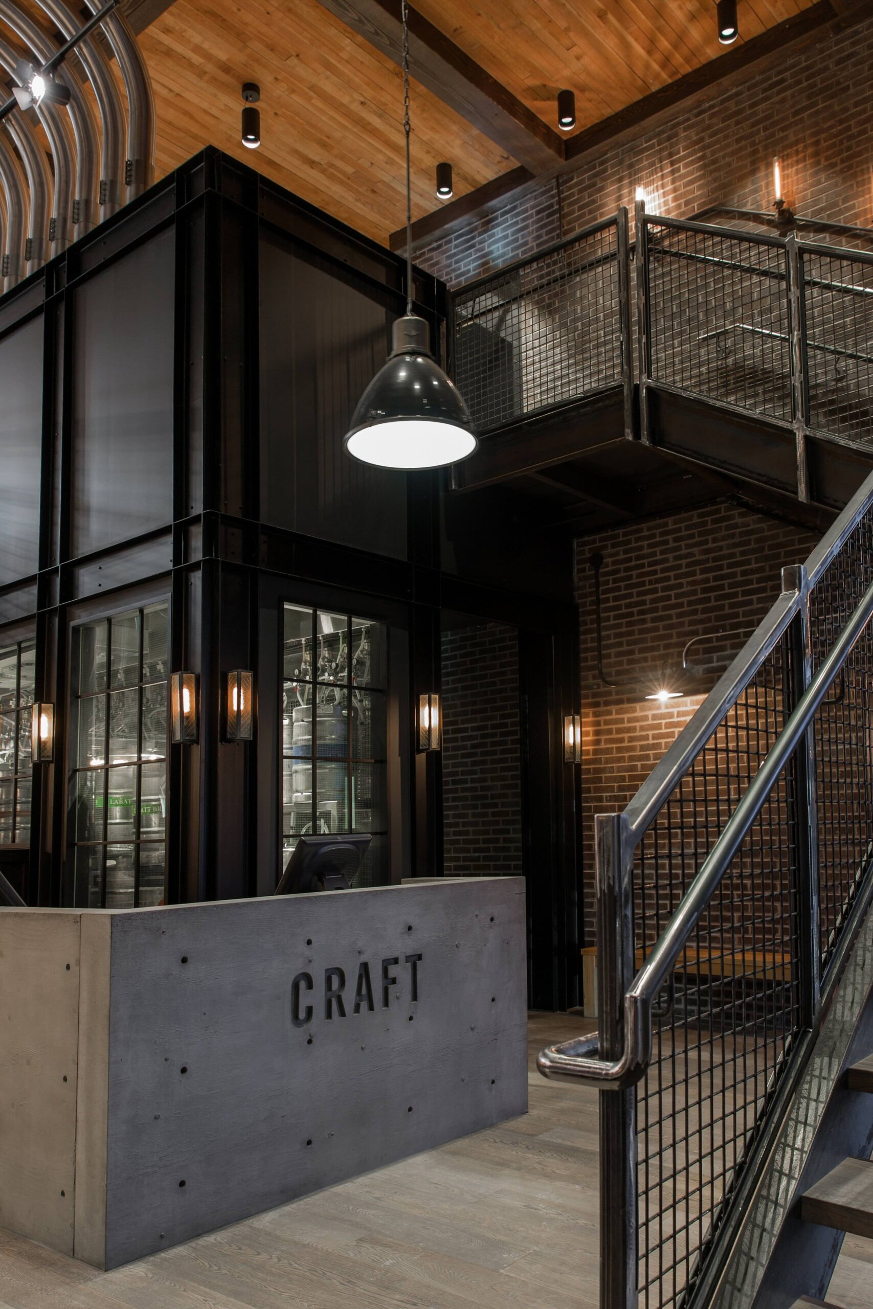 CRAFT Beer Market Industrial-style office lobby with exposed brick walls, metal railings, wood ceiling, modern light fixtures, and a concrete reception desk labeled "CRAFT.