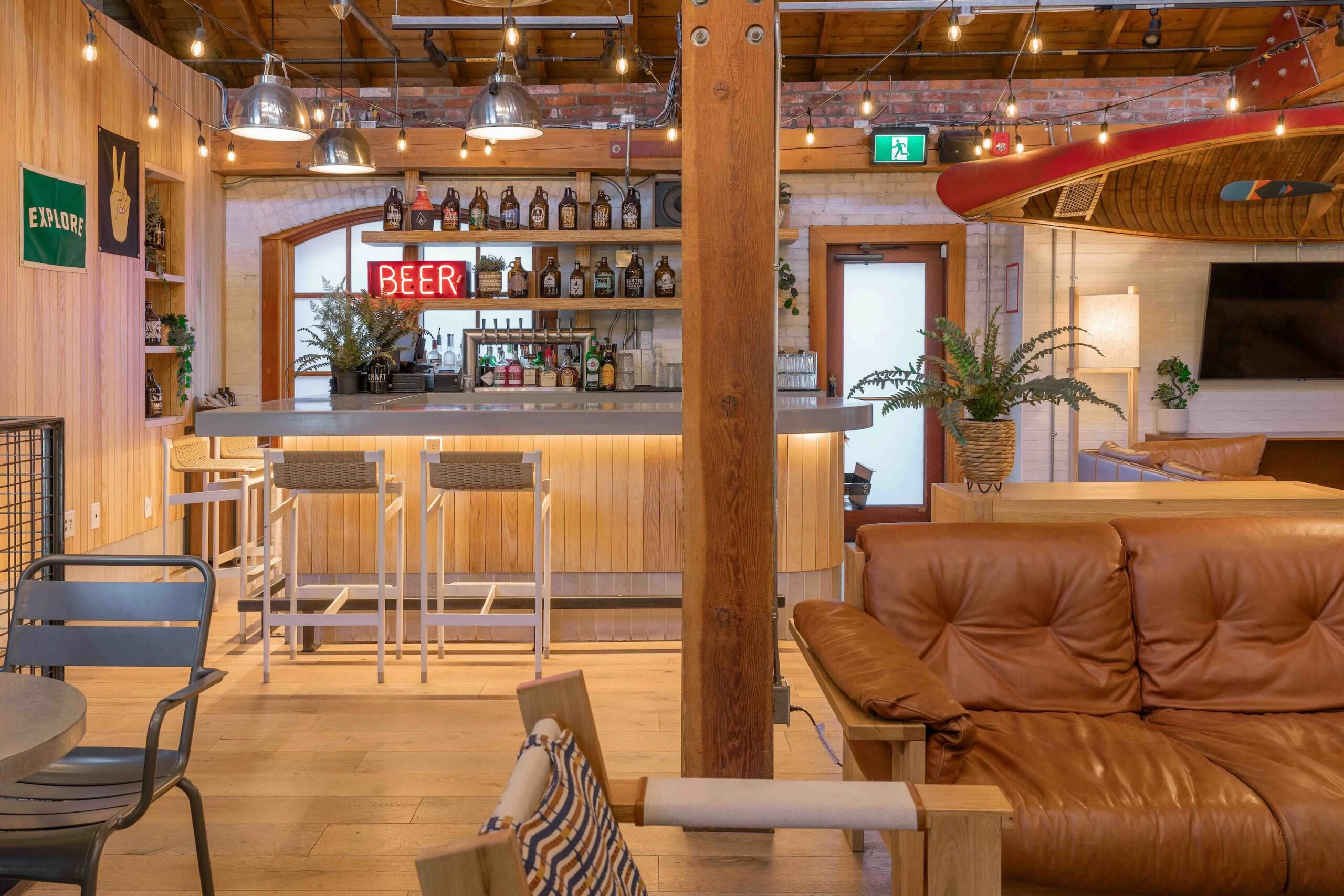 CRAFT Beer Market A modern bar area with wooden flooring, high stools, shelves of bottles, a red "BEER" sign, plants, and brown leather seating creates relaxed social vibes perfect for craft beer lovers in a well-lit space.