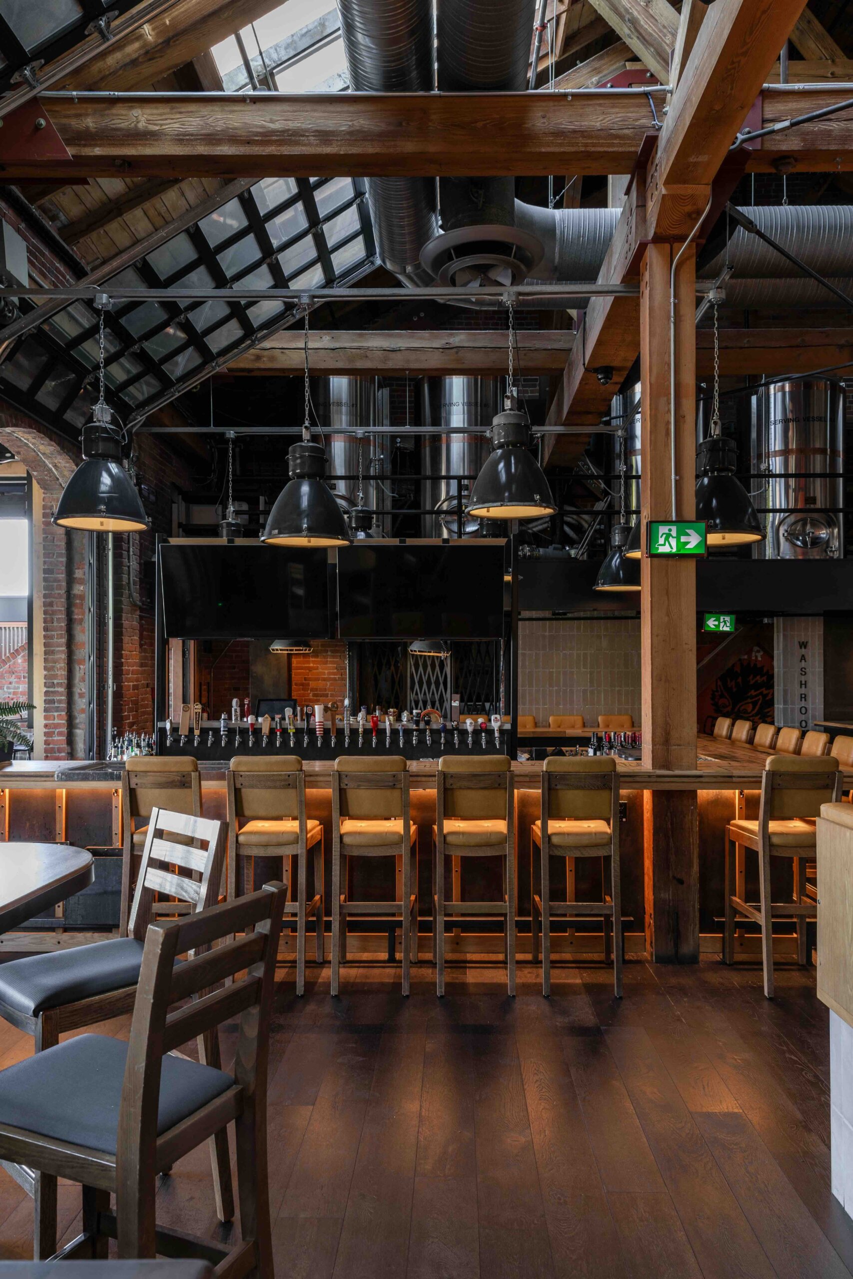 CRAFT Beer Market Modern industrial-style bar interior with wooden beams, hanging black lamps, high stools at the bar counter, and a visible ceiling with exposed ducts.