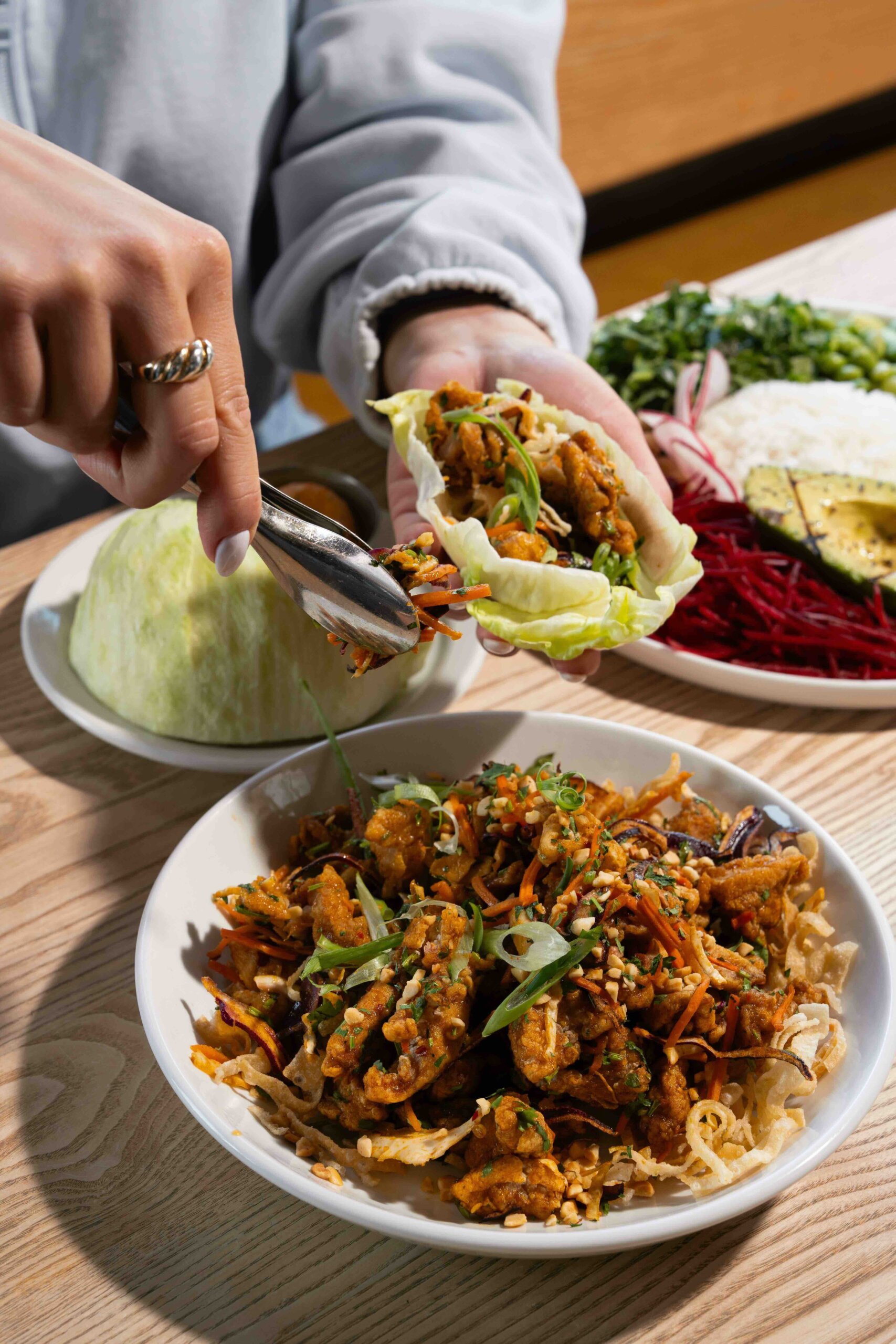 CRAFT Beer Market A person uses tongs to place crispy vegetable fritters into a lettuce leaf, with a bowl of fritters and a plate of shredded vegetables on the table.