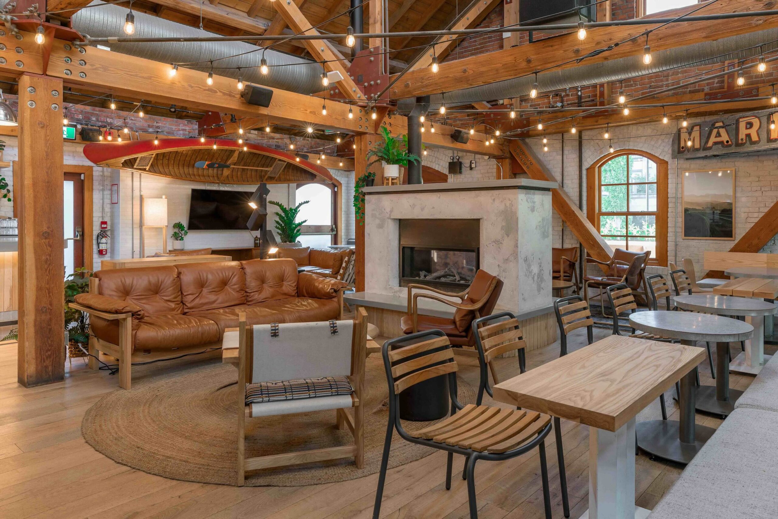 CRAFT Beer Market Spacious lounge with wooden beams, modern furniture, a central fireplace, and string lights. Large windows provide natural light, creating perfect social vibes for casual dining or enjoying a craft beer.