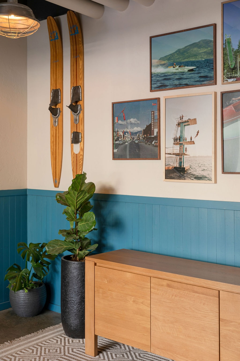 CRAFT Beer Market A wooden cabinet stands against a blue and white wall, with framed photos, two vintage wooden skis, and potted plants nearby.