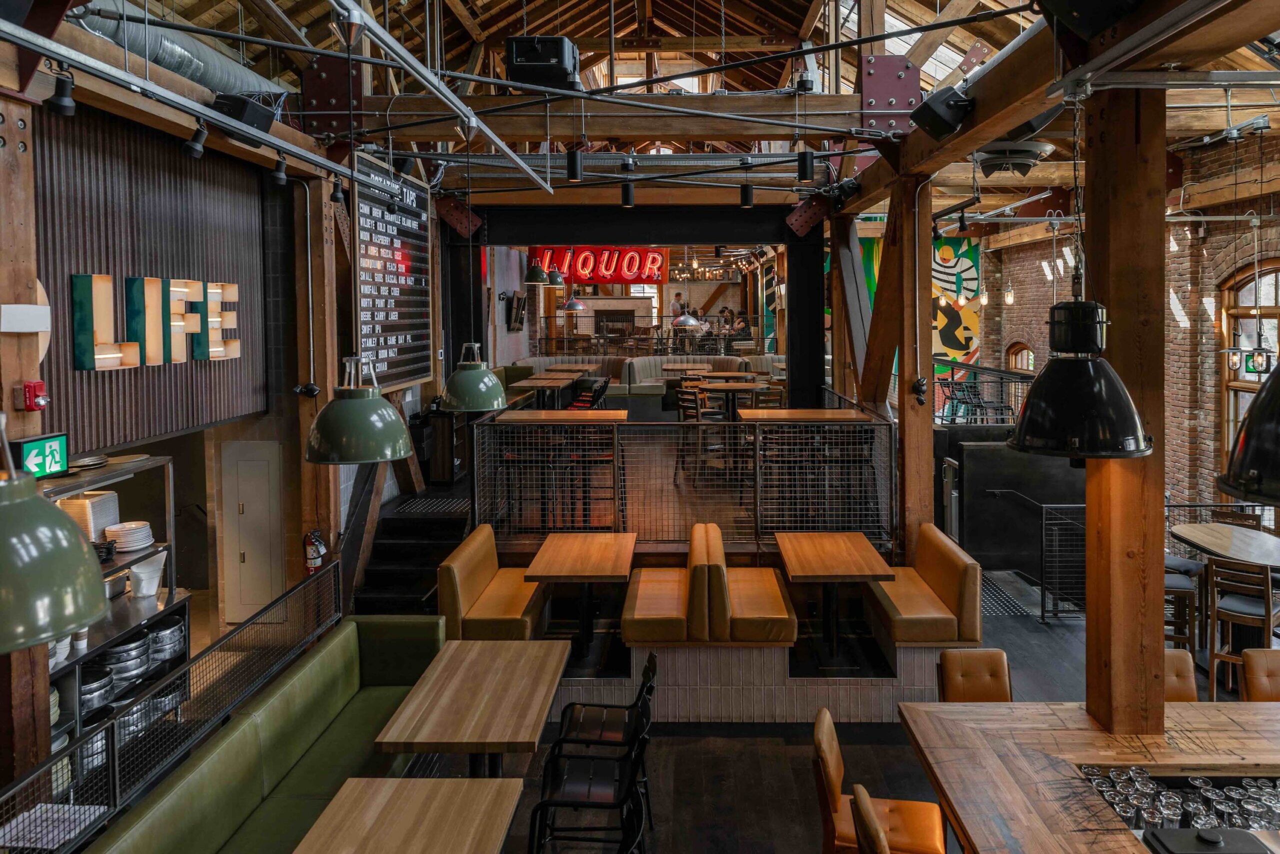 CRAFT Beer Market Spacious industrial-style restaurant interior with wooden tables, booths, hanging lights, exposed beams, and signs reading “LIFE” and “LIQUOR.” Perfect for casual dining and enjoying a craft beer with friends.