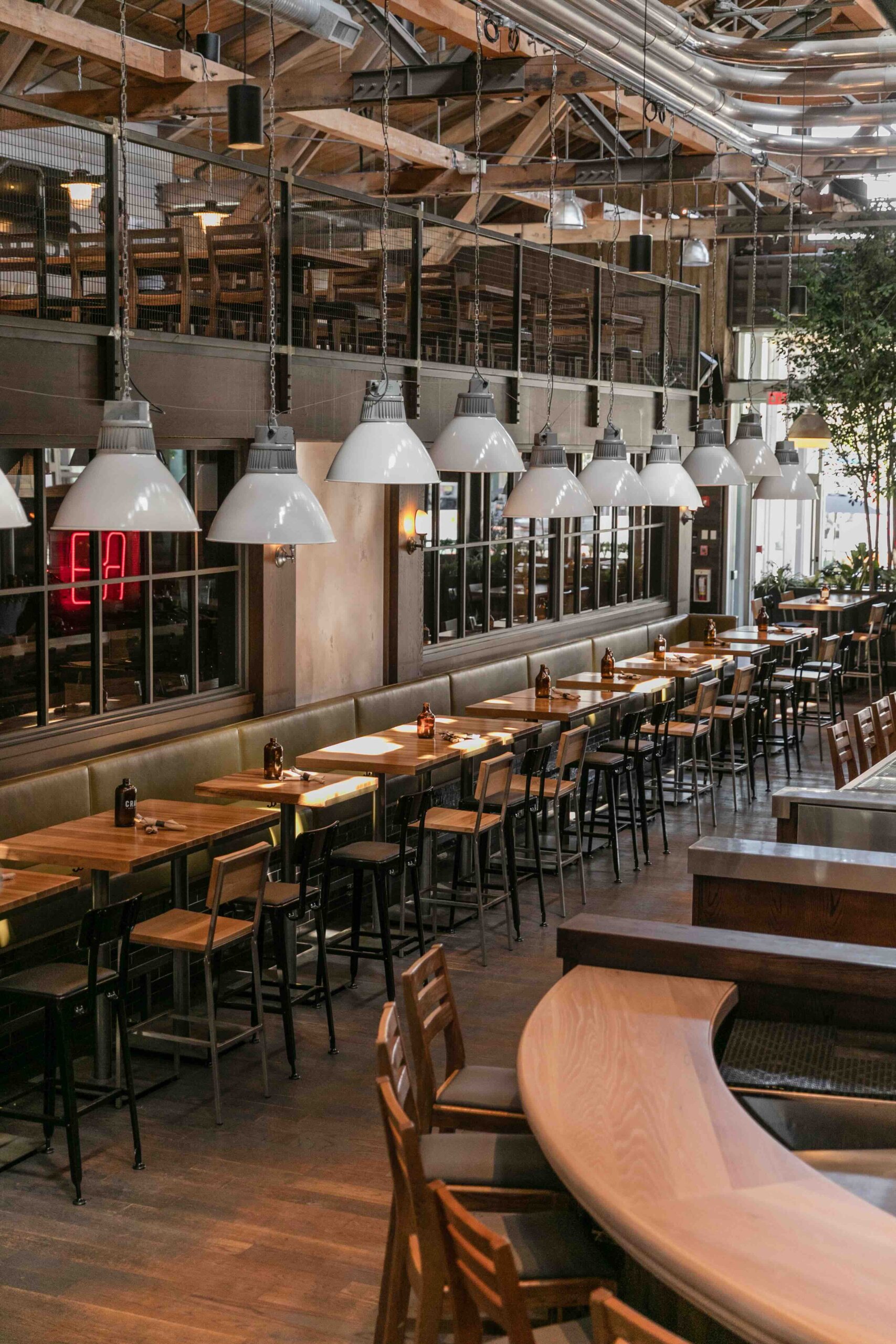 CRAFT Beer Market Spacious restaurant interior with wooden tables and chairs, large industrial pendant lights, high ceilings, an upper mezzanine seating area, and a casual dining vibe—perfect for enjoying craft beer with friends.