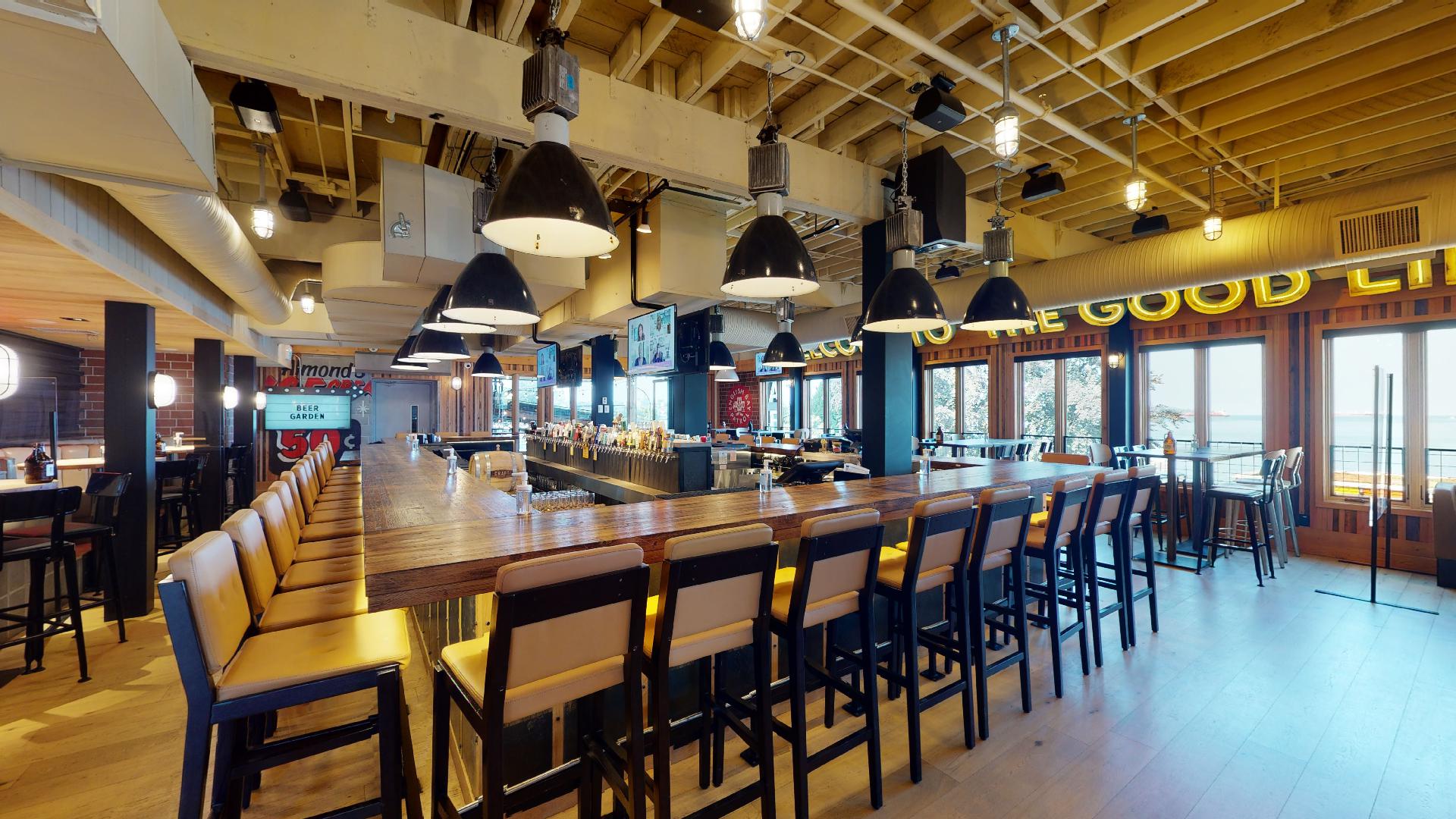 CRAFT Beer Market A spacious bar with high wooden stools, pendant lights, multiple TV screens, and large windows letting in natural light.